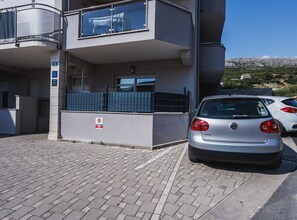 Um edifício moderno com varanda, um Volkswagen Golf estacionado na frente e uma placa de proibido estacionar no chão.