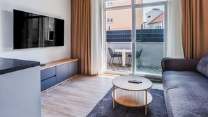 Moderni olohuone, jossa on litteänäyttöinen televisio, sohva, sohvapöytä ja liukuovi, joka johtaa ulkotilalle.