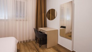 Hotellihuone, jossa on sänky, työpöytä, tuoli, peili ja ikkuna, jossa on verhot.