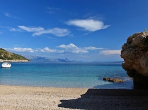 Ein Kiesstrand mit klarem Wasser, einem Boot und fernen Bergen.