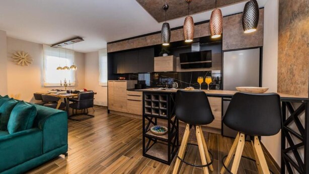 Una cocina moderna con suelo de madera, un comedor con sofá verde y una zona de bar con taburetes.