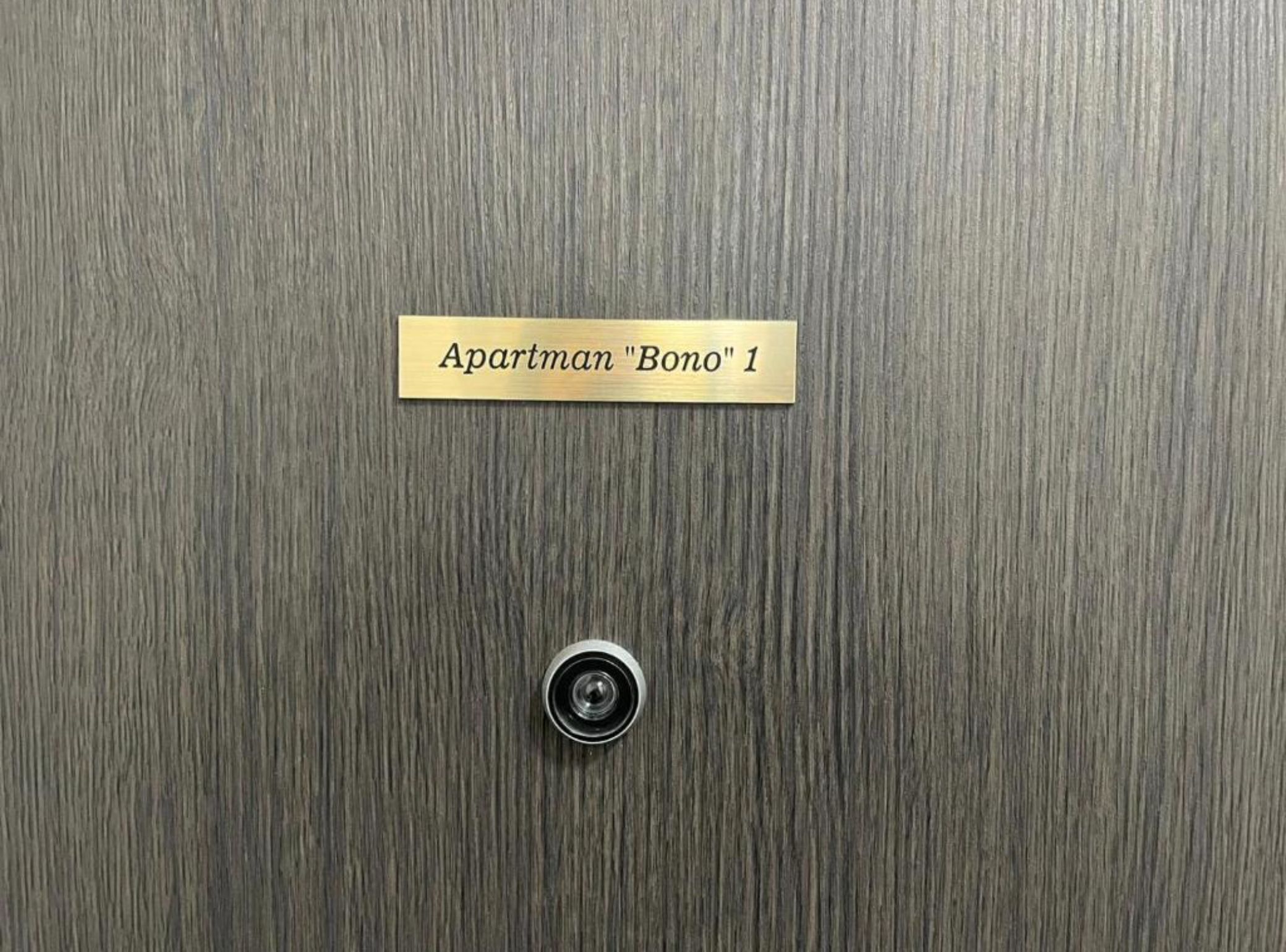 A door with a brass plate labeled 'Apartman 'Bono' 1' and a keyhole below it.