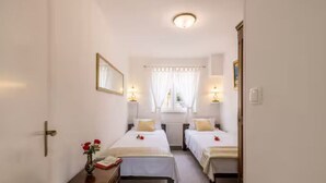 A hotel room with two beds, a bedside table with a vase of flowers, a window with curtains, and a ceiling light. - Villa Pax (Lovreć)