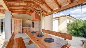 An outdoor wooden dining area with benches and a table, a brick fireplace, and a view of a house and greenery. - Guest House Gabriel (Vodnjan)