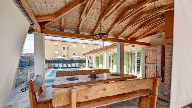 A wooden dining table with benches, a pool, and a building in the background. - Guest House Gabriel (Vodnjan)