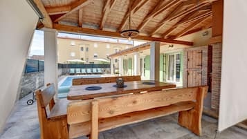A wooden dining table with benches, a pool, and a building in the background.