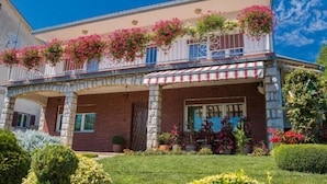 Ein zweistöckiges Gebäude mit einem Balkon, der mit hängenden Blumenkästen geschmückt ist, einem steinernen Bogenportal und einem gepflegten Garten.