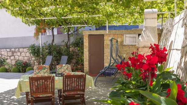 Eine Terrasse im Freien mit Tisch, Stühlen, einer Steinmauer und Blumentöpfen.
