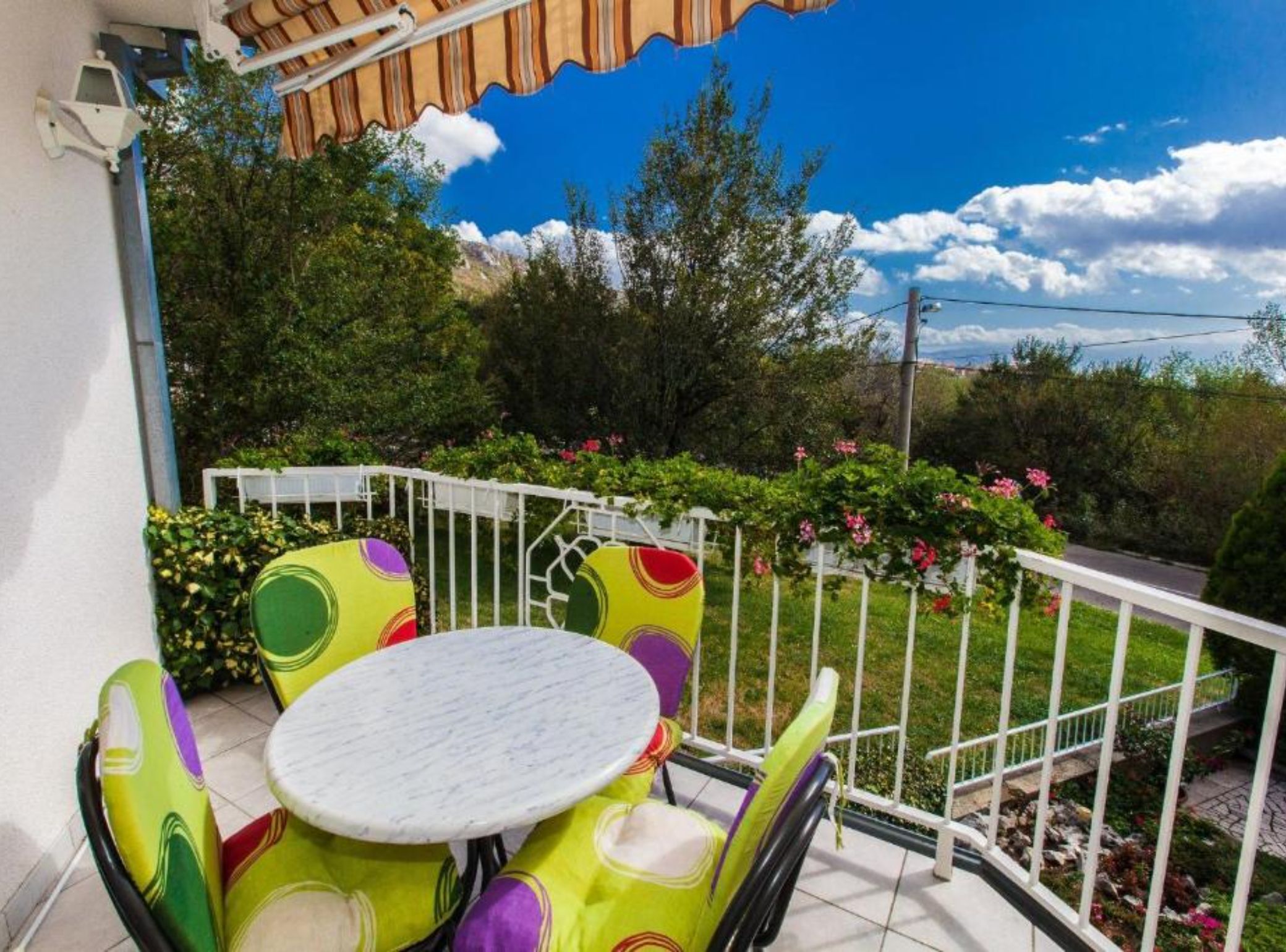 Un balcon avec une balustrade blanche, une table ronde et des chaises colorées.