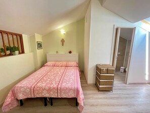 Un dormitori amb llit, una taula de nit, una làmpada de paret, una planta en test i una porta que condueix a un bany.