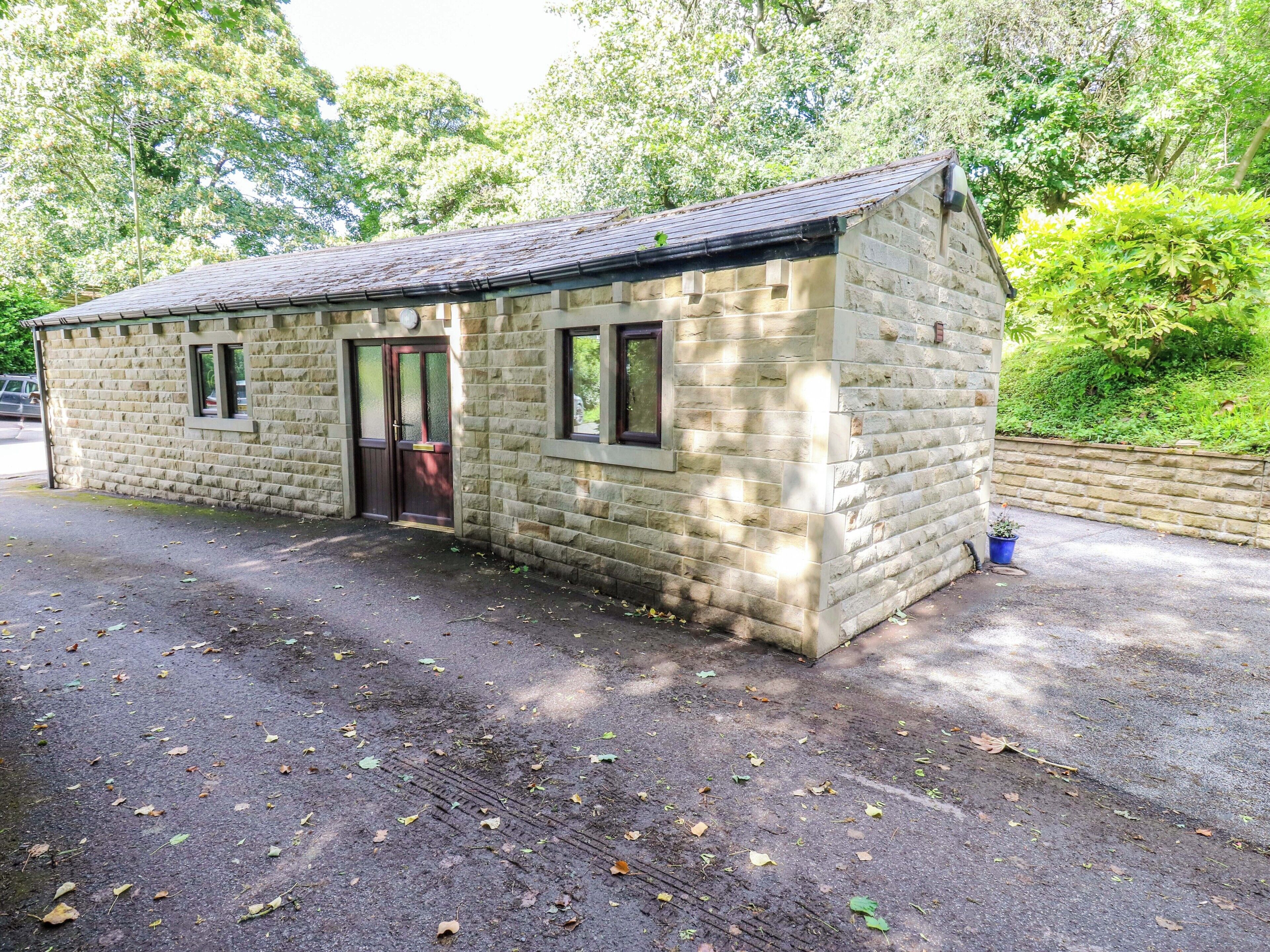 A small stone building with a door and windows, surrounded by trees and a paved area.