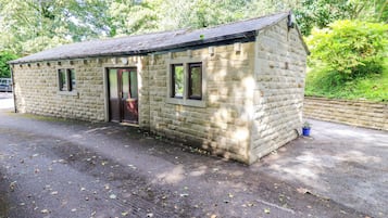 A small stone building with a door and windows, surrounded by trees and a paved area.