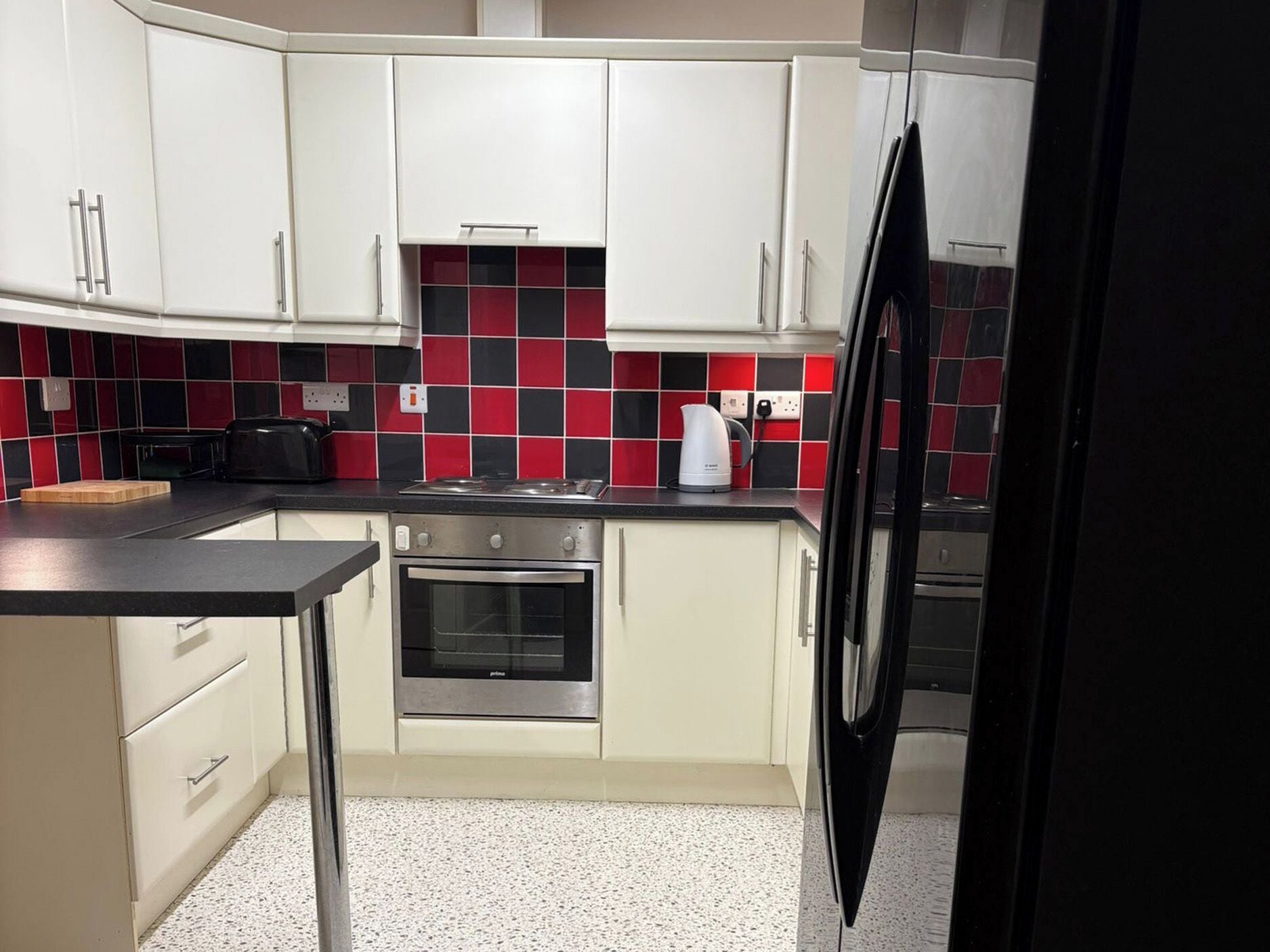 A kitchen with white cabinets, a black countertop, a stove, an oven, and a kettle.