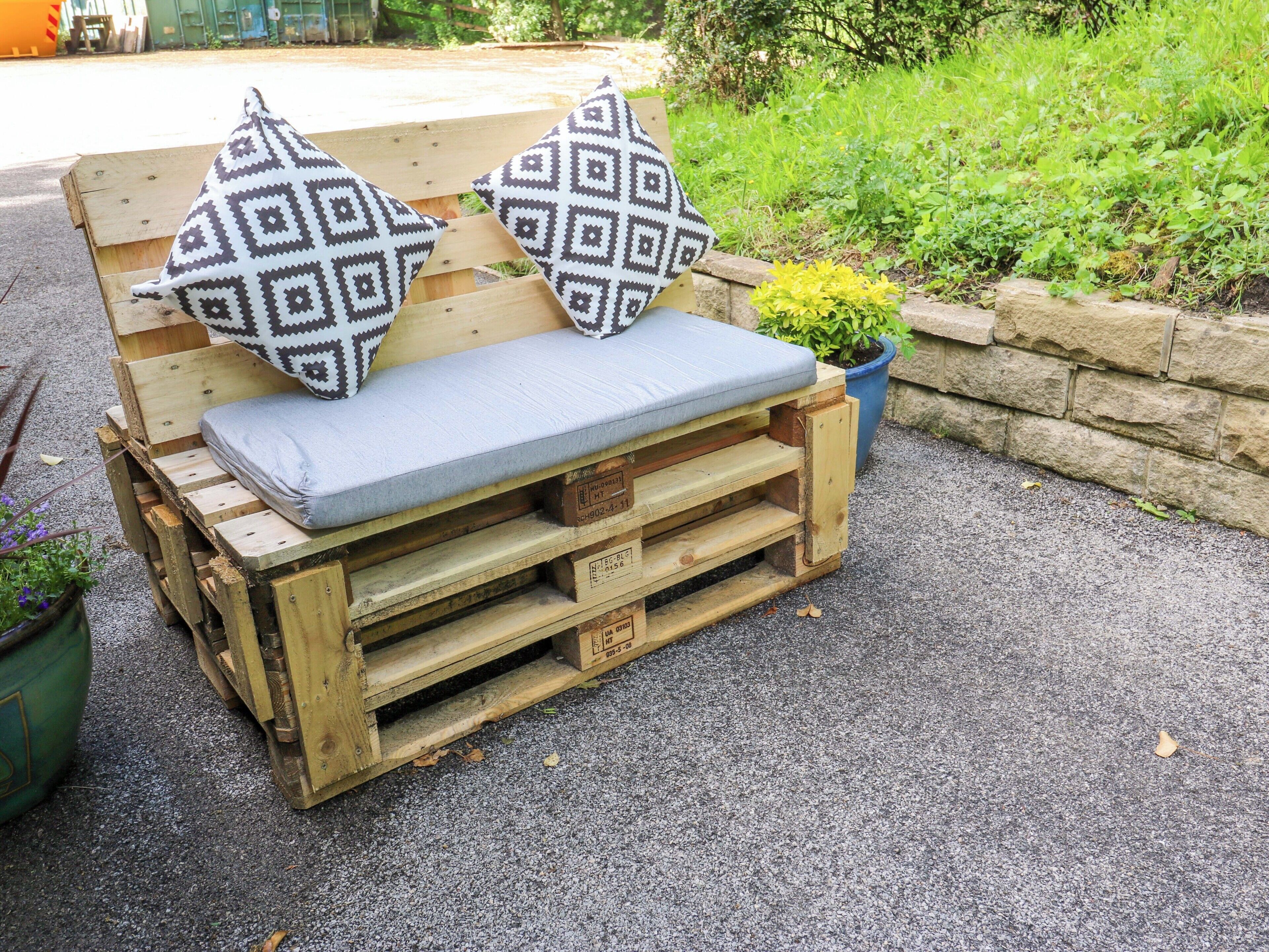 A wooden bench with cushions and a small potted plant.