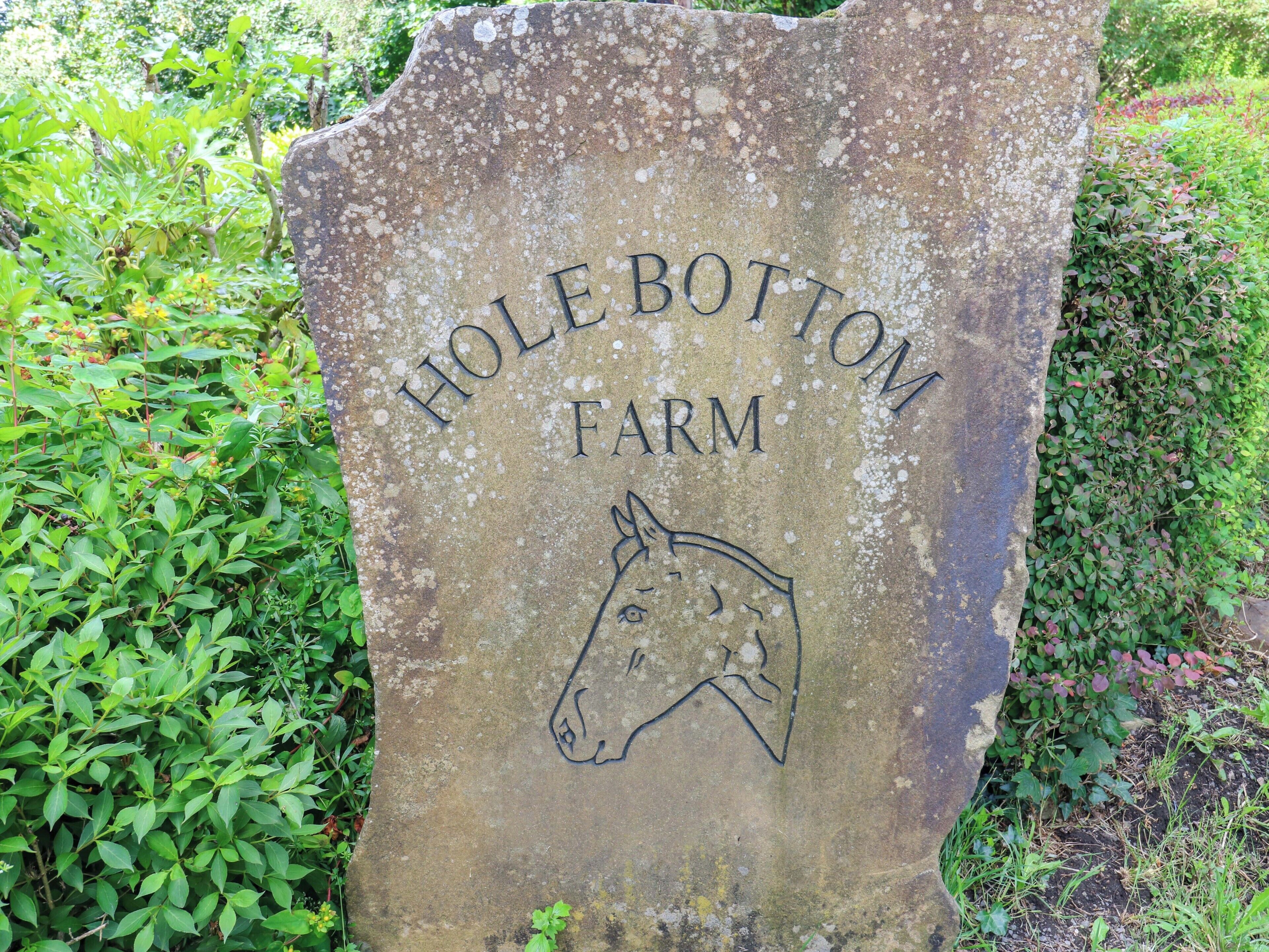 Ein Steinschild mit der Aufschrift 'HOLEBOTTOM FARM' und einer eingravierten Pferdekopf-Darstellung.