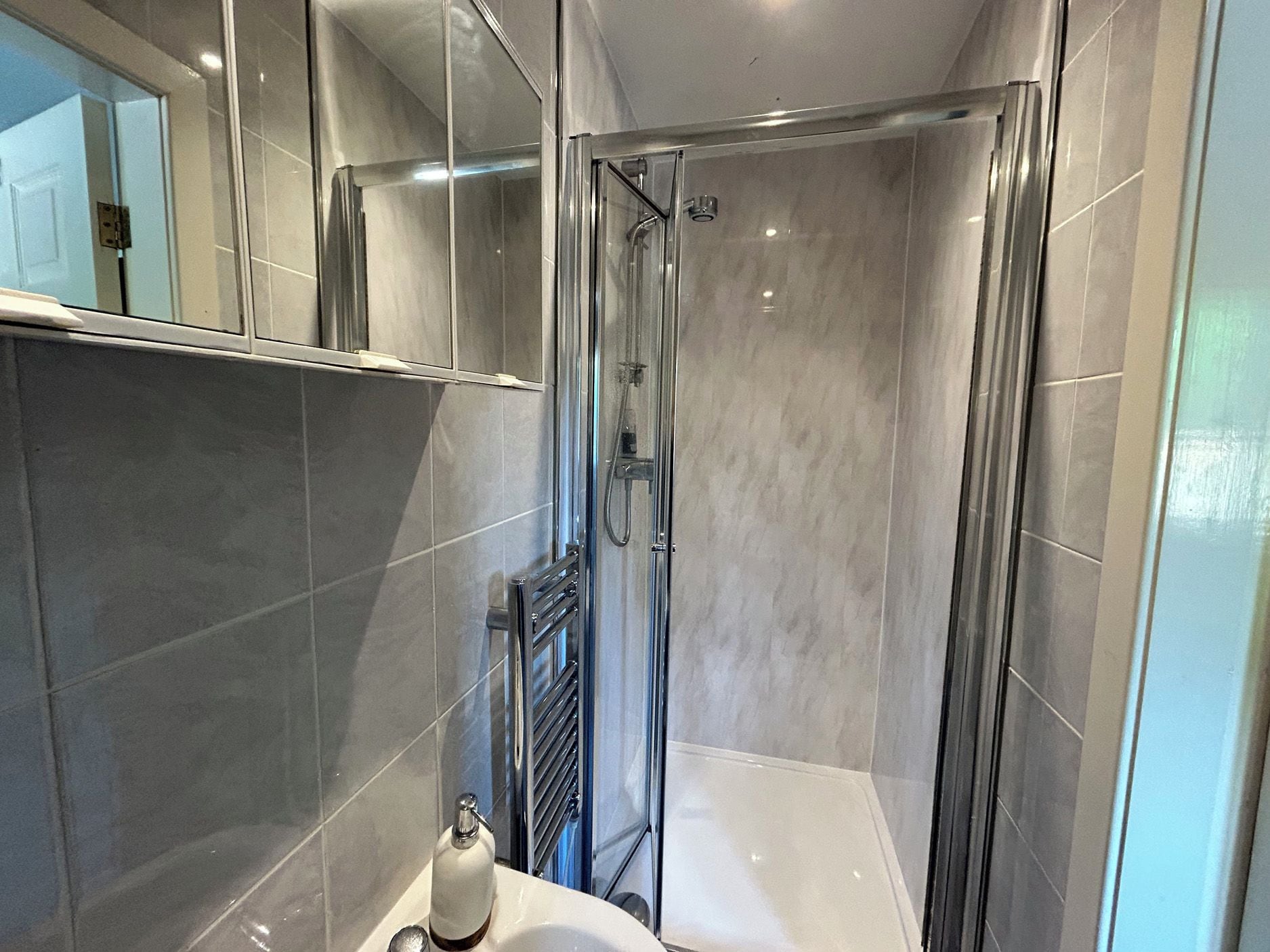 A modern bathroom with a glass shower enclosure, a white sink, and a towel rack.