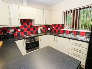 A kitchen with white cabinets, a black and red tiled backsplash, a stainless steel sink, and a window with blinds. - The Lodge (Brighouse)