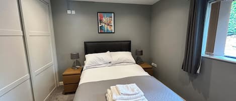A neatly made bed with a folded towel, a nightstand with a lamp, and a framed picture on the wall.