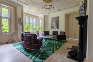 Una habitación con chimenea, un tapete verde estampado y un ventanal con vistas a la vegetación.