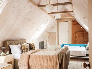 Un dormitorio con techo inclinado, una cama, un aparador, un radiador y una pared de ladrillo.