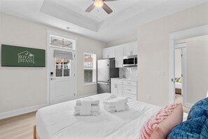 A hotel room with a bed, a ceiling fan, a kitchenette, and a door leading to another room. - The Sail Away | Near Beach & Boardwalk (Myrtle Beach)