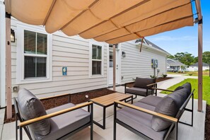 An outdoor patio with a covered seating area, a table, and a house in the background. - The Sail Away | Near Beach & Boardwalk (Myrtle Beach)