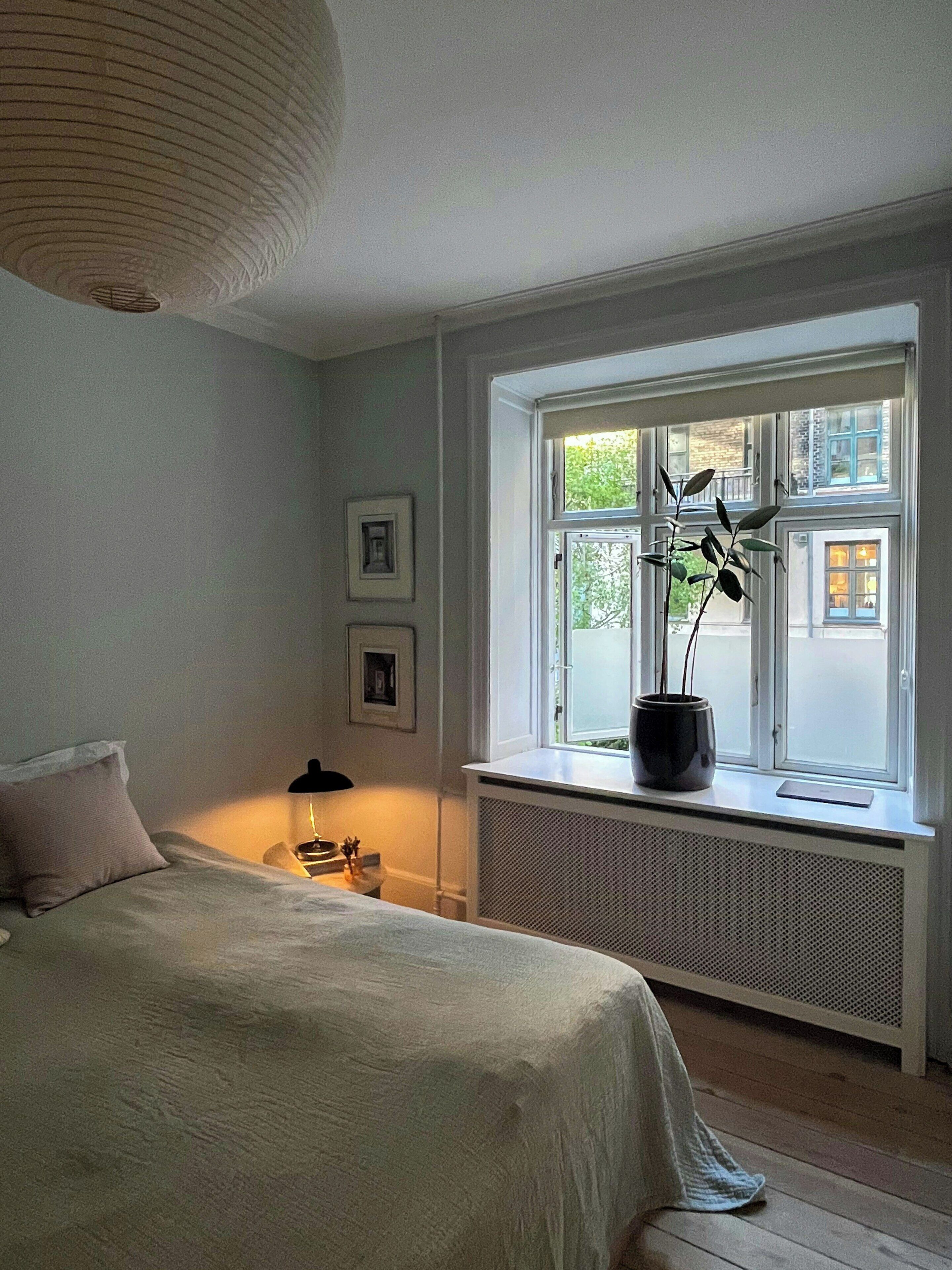 Et soveværelse med seng, et vindue med udsigt, en radiator og et natbord med lampe.
