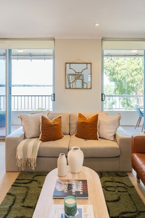 A living room with a sofa, a coffee table, and a view through large windows. - Casa Lune- sweeping Swan river views. Steps to iconic Blue Boat house and CBD. (Crawley)