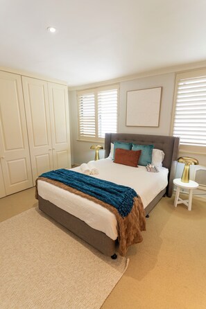 A bedroom with a large bed, a bedside table, a nightstand, a window with blinds, and a door. - Blue House & River views Spectacular and x large apartment 2bd 6pp (Crawley)