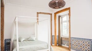Ein Schlafzimmer mit einem Himmelbett, Holzboden, einer Wand mit Muster und einer hängenden Leuchte.