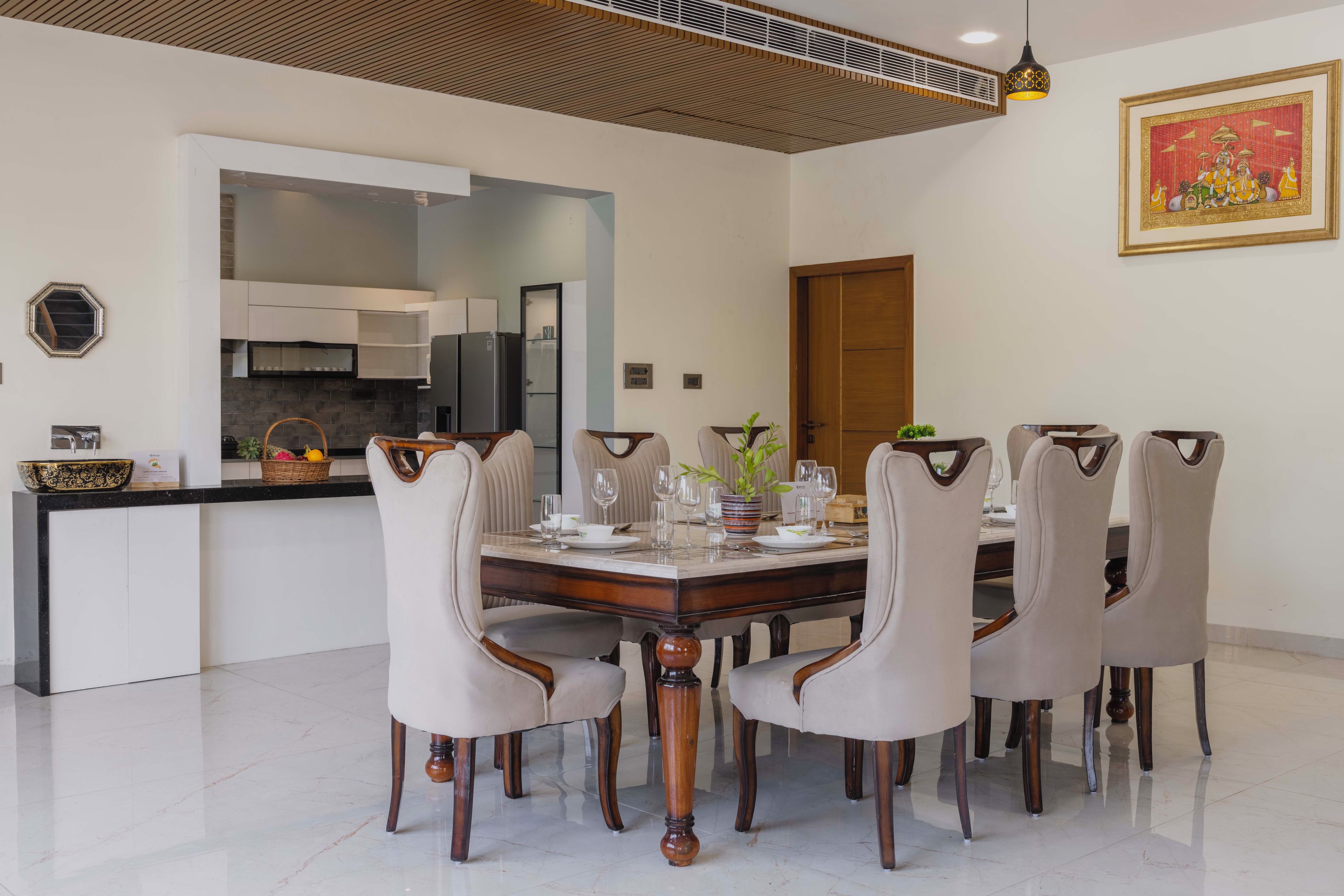A dining area with a round table, six chairs, and a kitchen in the background.