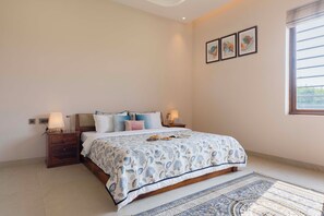 A bedroom with a bed, nightstands, a window, and a wall with three framed pictures. - ELIVAAS Lush Haven 4BHK Villa Pvt Pool (Jaipur)