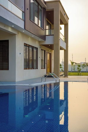 A modern building with a swimming pool, large windows, and a balcony. - ELIVAAS Lush Haven 4BHK Villa Pvt Pool (Jaipur)