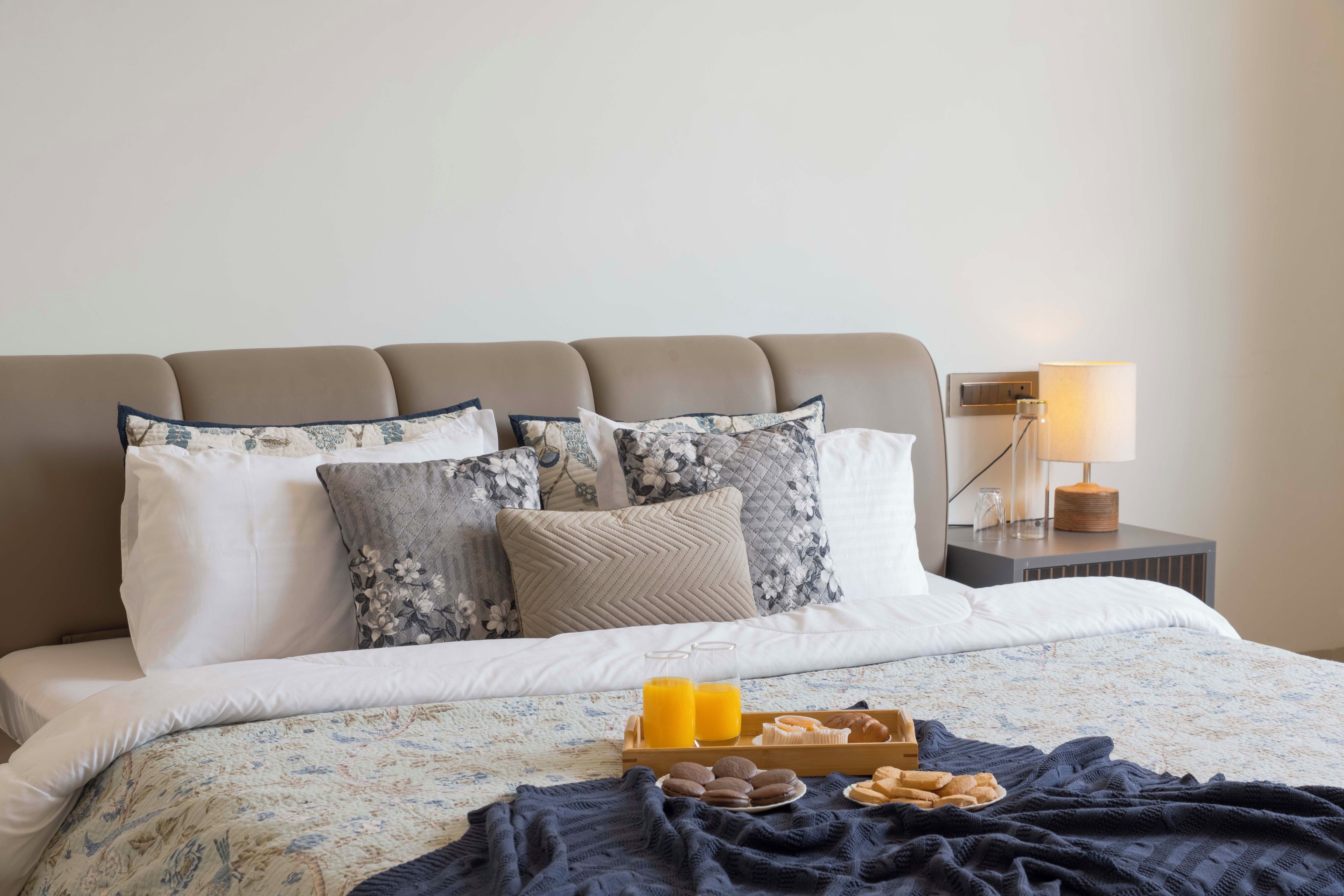 Una cama bien hecha con ropa de cama floral, una bandeja con alimentos para el desayuno y una lámpara de noche.