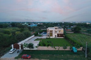 A modern two-story house with a large lawn, a swimming pool, and a car parked in the driveway. - ELIVAAS Lush Haven 4BHK Villa Pvt Pool (Jaipur)