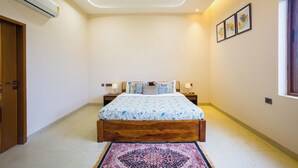 Une chambre à coucher comprenant un lit, deux tables de chevet, un climatiseur, une fenêtre avec des rideaux et une porte.