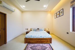 A bedroom with a bed, two bedside tables, an air conditioner, a window with curtains, and a door. - ELIVAAS Lush Haven 4BHK Villa Pvt Pool (Jaipur)