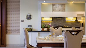 Un coin repas avec une table dressée pour quatre personnes, une cuisine en arrière-plan et une plante en pot sur le comptoir.