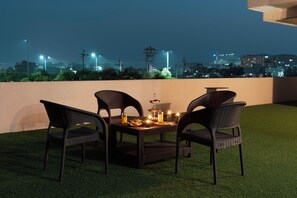 A rooftop terrace with a table set for two, surrounded by wicker chairs, and a cityscape view in the background. - ELIVAAS Lush Haven 4BHK Villa Pvt Pool (Jaipur)