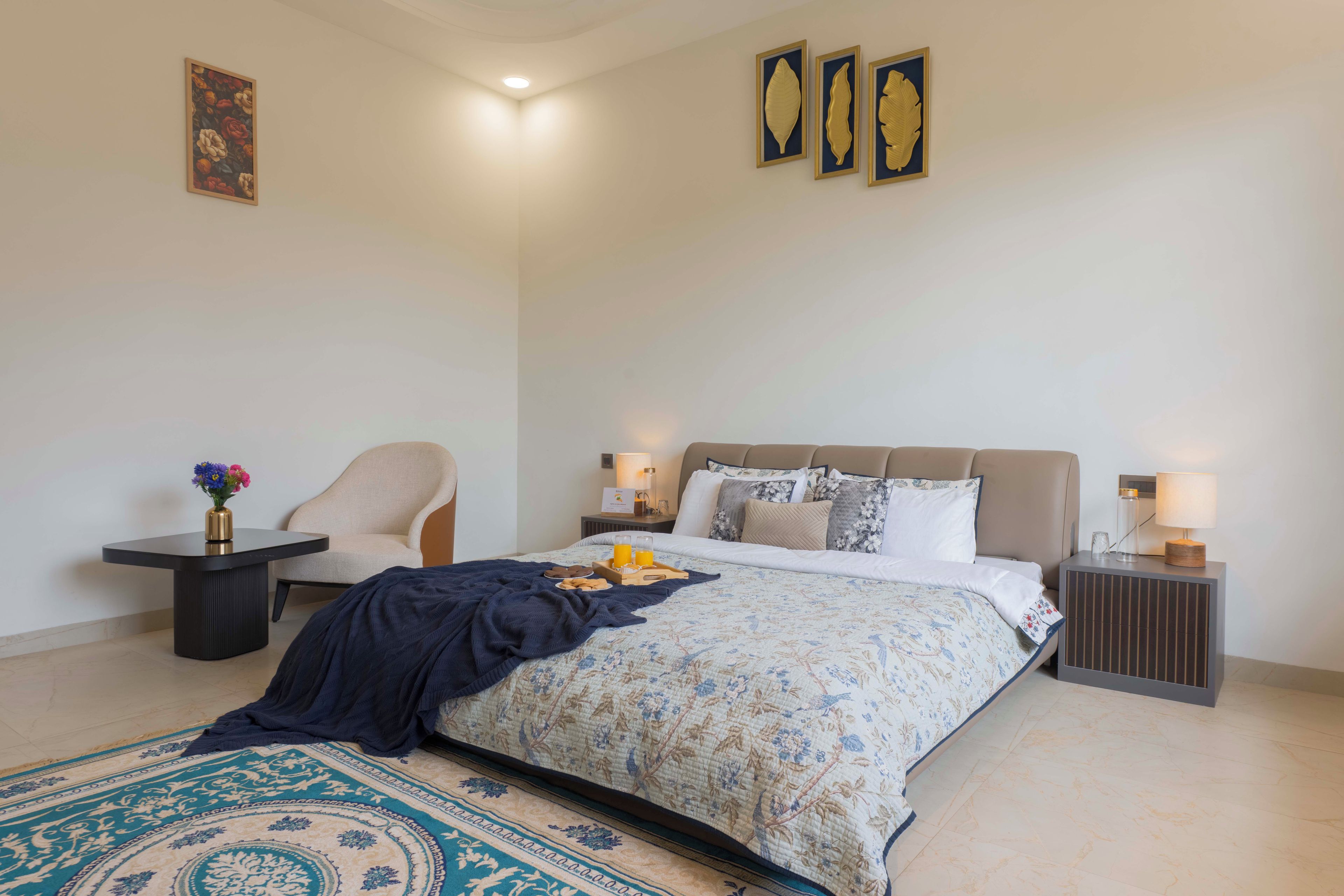 A well-lit bedroom with a bed, a chair, a nightstand, and a bedside table.