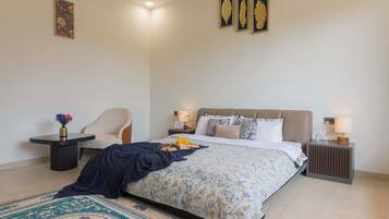 A well-lit bedroom with a bed, a chair, a nightstand, and a bedside table.