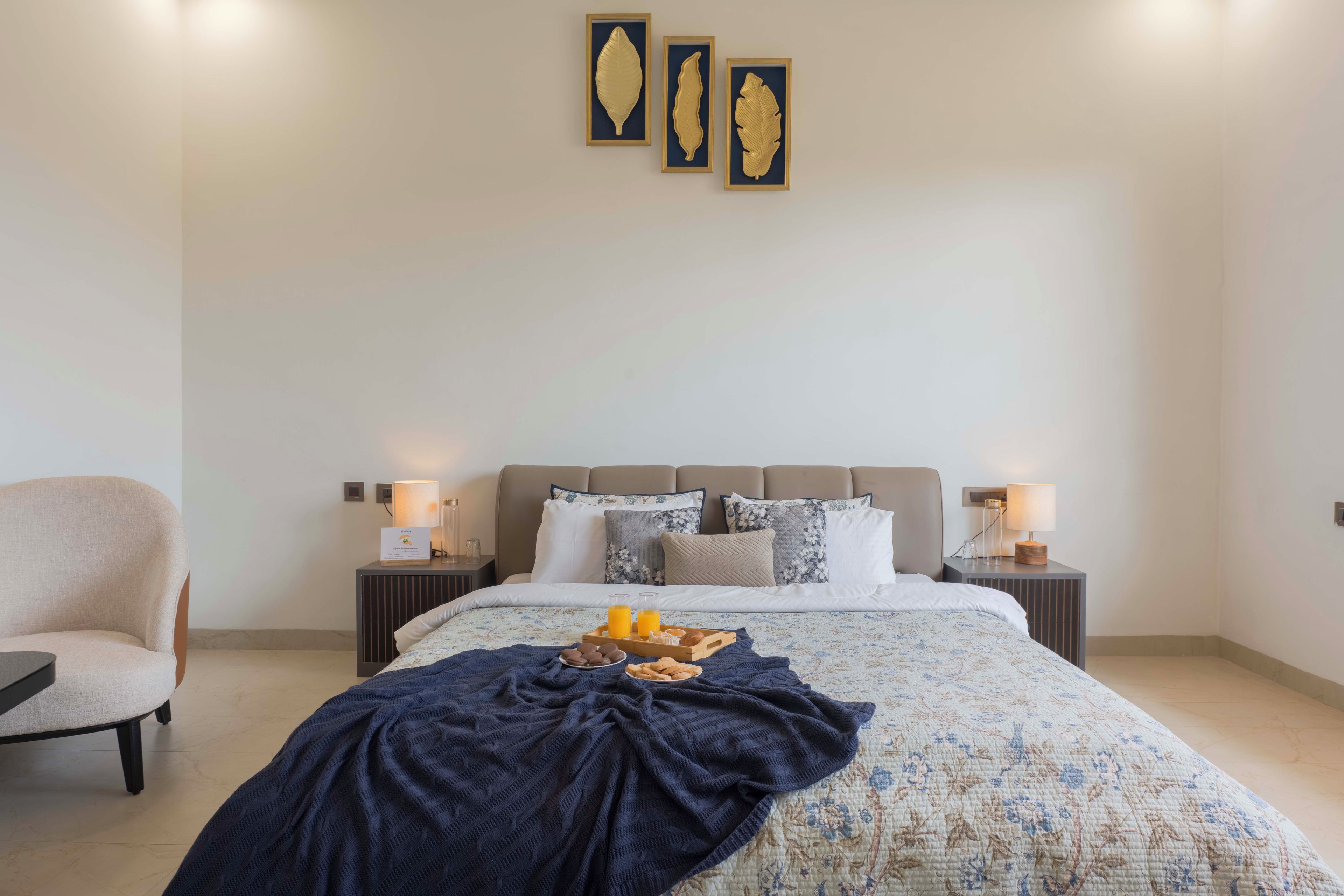 A hotel room with a bed, bedside tables, a chair, and artwork on the wall.