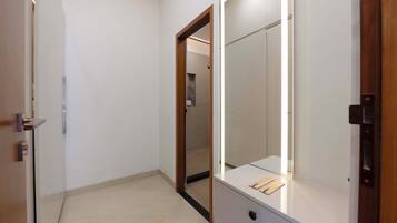 A hallway with a door leading to a bathroom, a mirror, and a small table with items on it.