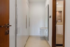 A narrow hallway with a wooden door on the left, a mirror on the right, and a small bathroom area with a sink and towel. - ELIVAAS Lush Haven 4BHK Villa Pvt Pool (Jaipur)