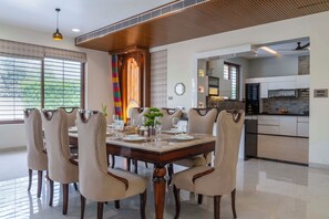 A dining area with a large wooden table, six chairs, and a decorative centerpiece. - ELIVAAS Lush Haven 4BHK Villa Pvt Pool (Jaipur)