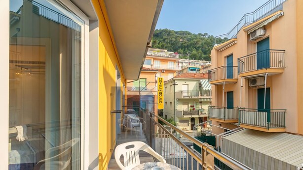 A balcony with a table and chairs, a glass door leading to a room, and a view of a hotel building in the background. - Hotel Del Golfo (Laigueglia)