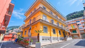 A multi-story yellow building with balconies, a clear sky, and a hilly background. - Hotel Del Golfo (Laigueglia)