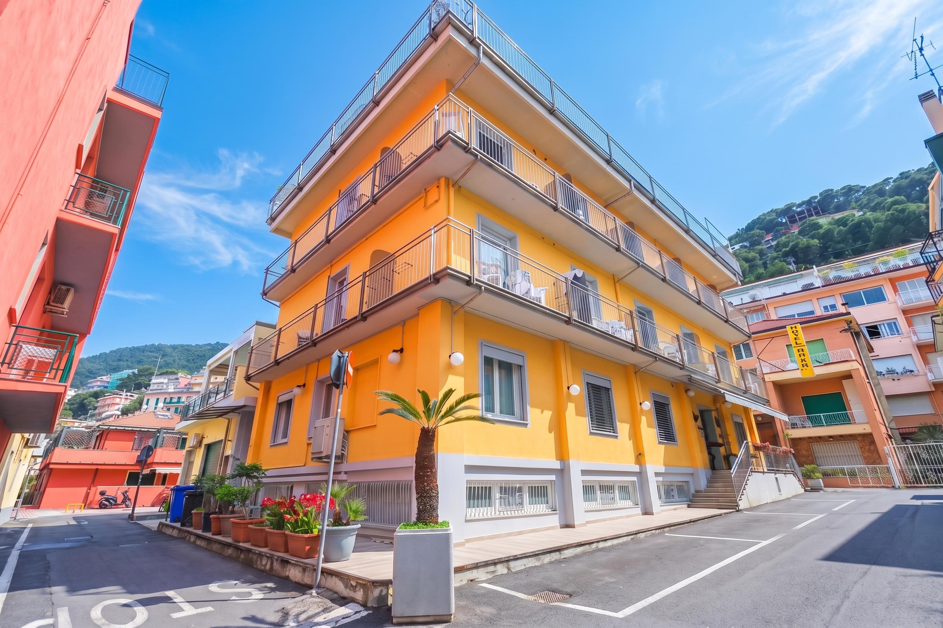 A multi-story yellow building with balconies, a clear sky, and a hilly background.
