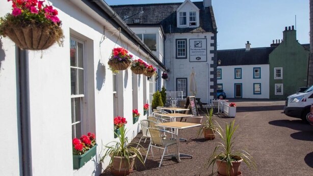 A building with hanging flower baskets, outdoor seating, and a sign indicating a hotel. - The Murray Arms Hotel (Castle Douglas)