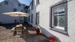 A courtyard with a wooden table and chairs, a beige umbrella, and potted plants. - The Murray Arms Hotel (Castle Douglas)